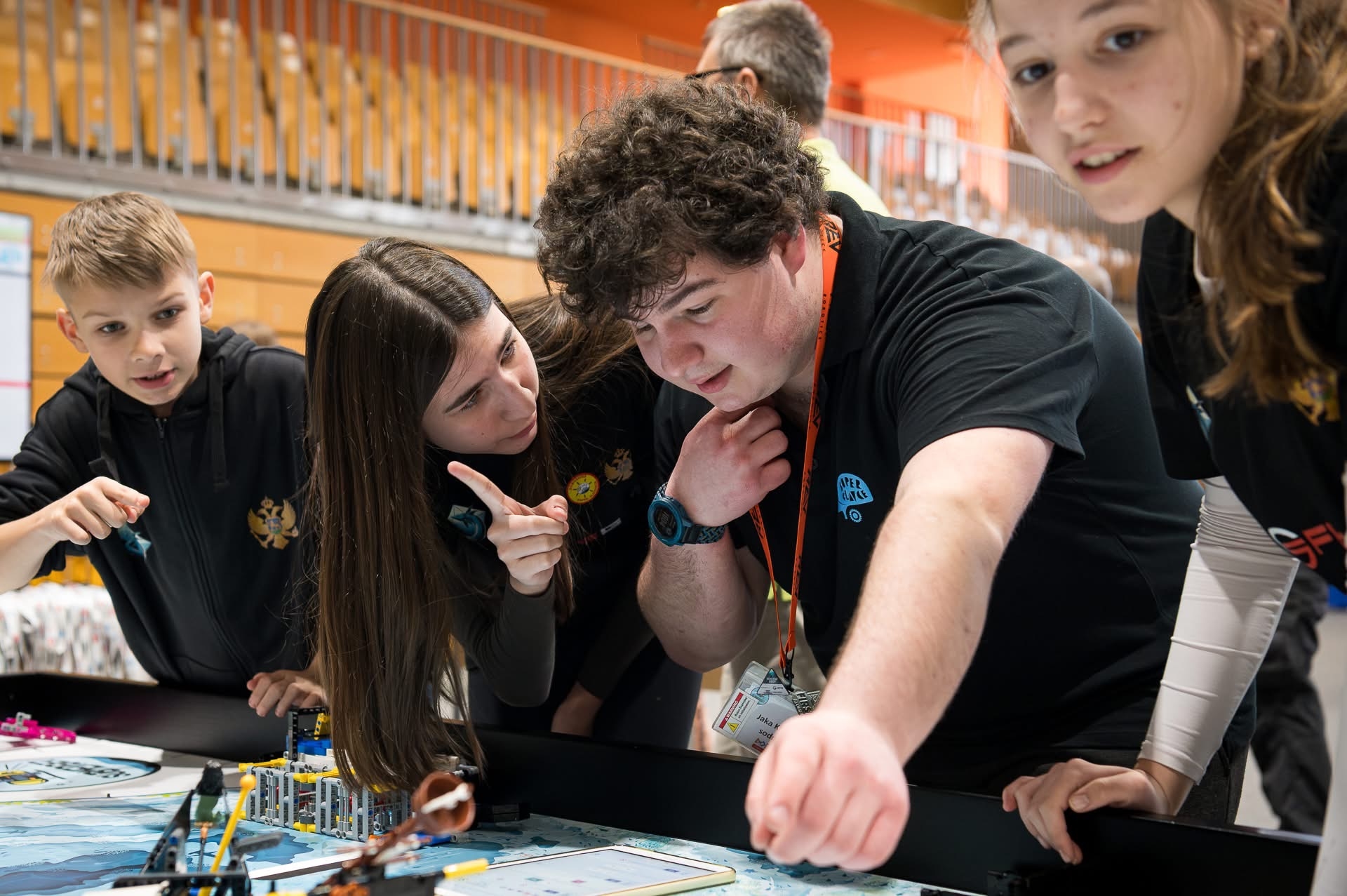 Članovi tima nagnuti nad stolom za robotsku igru dok prate misiju robota na FIRST LEGO League takmičenju